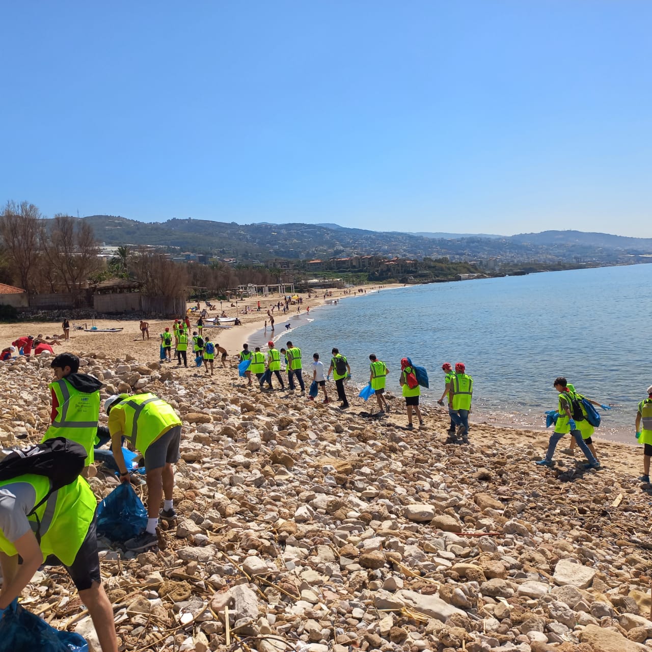 Volunteers in safety vests collecting trash along the beach in Byblos